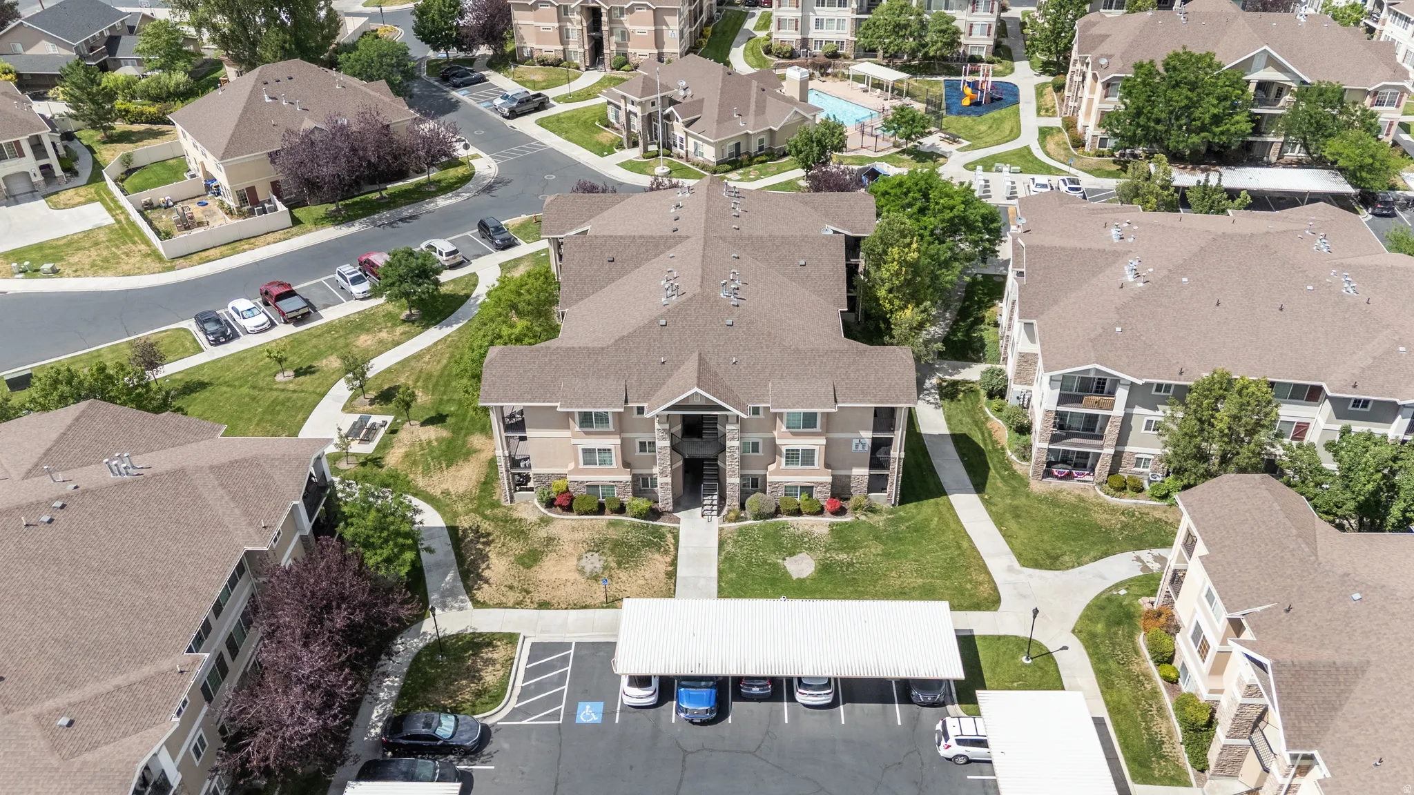Multi-level apartment building featuring a neutral-toned exterior, gabled roofline, covered parking, and an on-site swimming pool