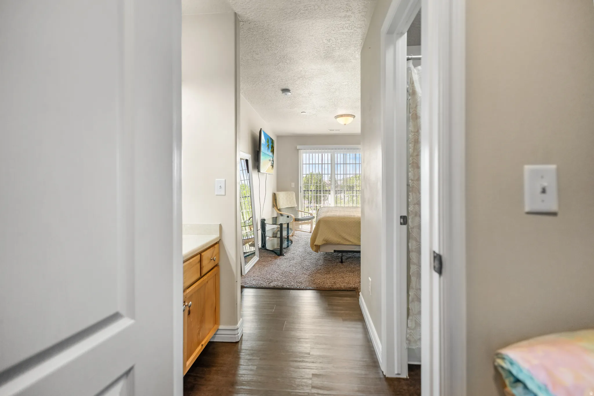 Hallway with wood-finish flooring leading to a bedroom with carpeted flooring