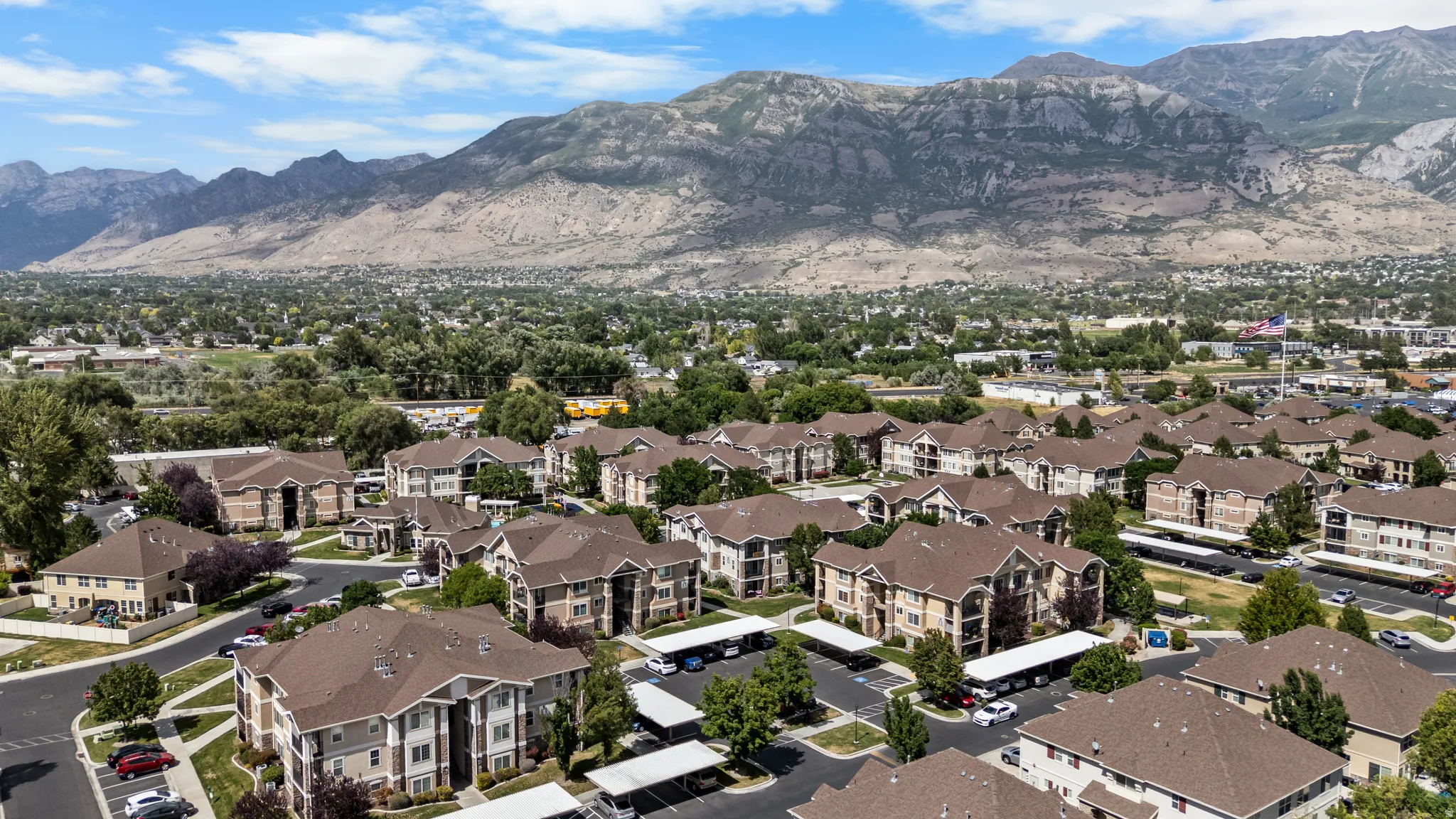 Expansive residential development with numerous multi-story buildings, consistent architectural design, covered parking structures, mature trees, and mountainous scenery