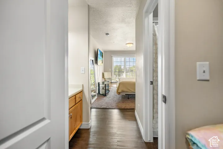 Hallway with wood-finish flooring leading to a bedroom with carpeted flooring