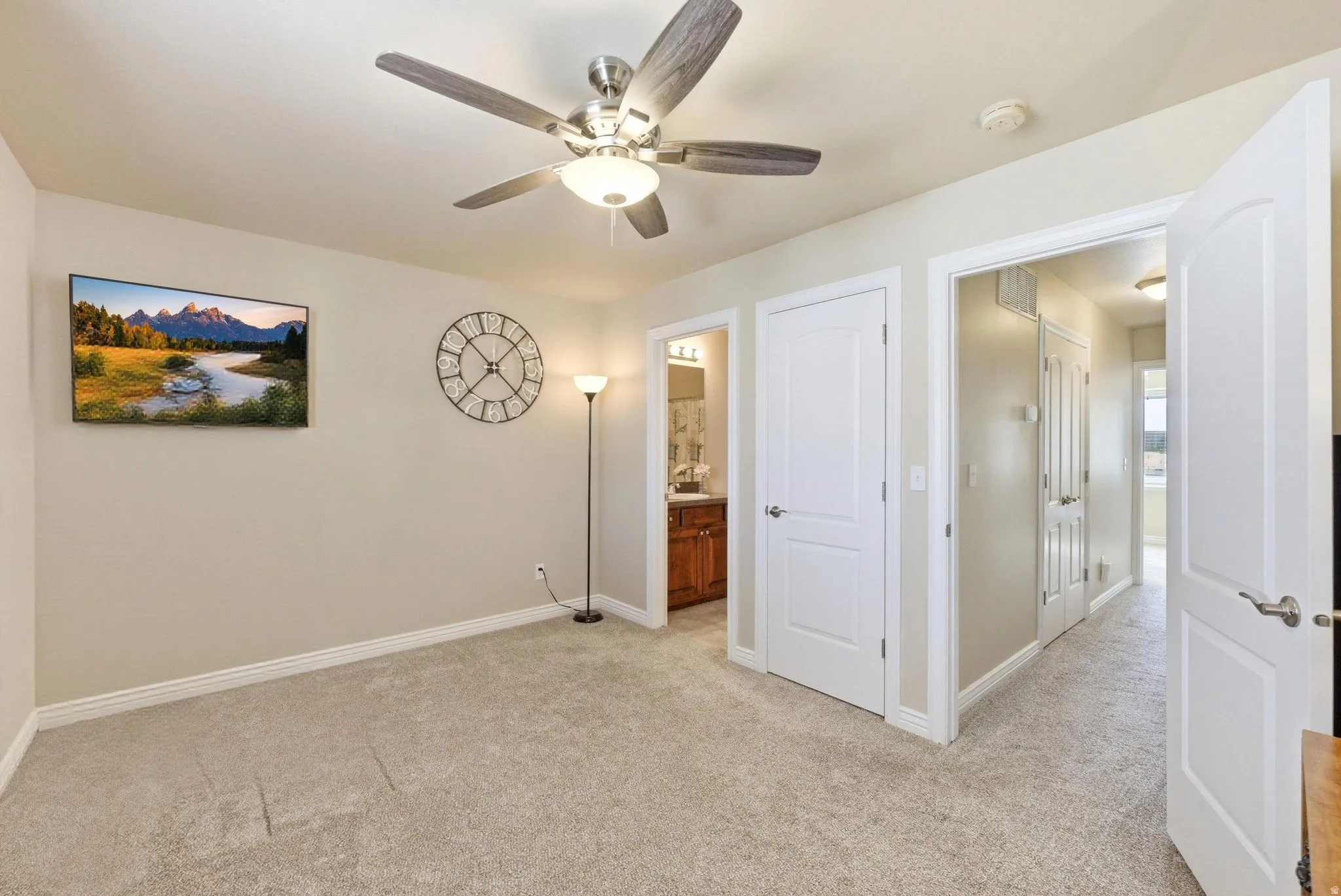 Unfurnished bedroom featuring light carpet, ensuite bath, and a ceiling fan