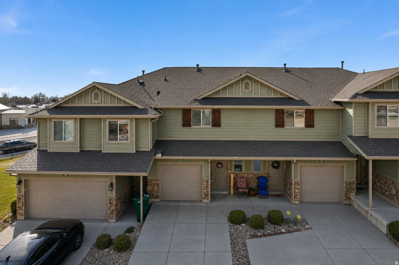 Townhome-style property featuring a light green siding exterior, dark shingle roofing, and attached garages with concrete driveways