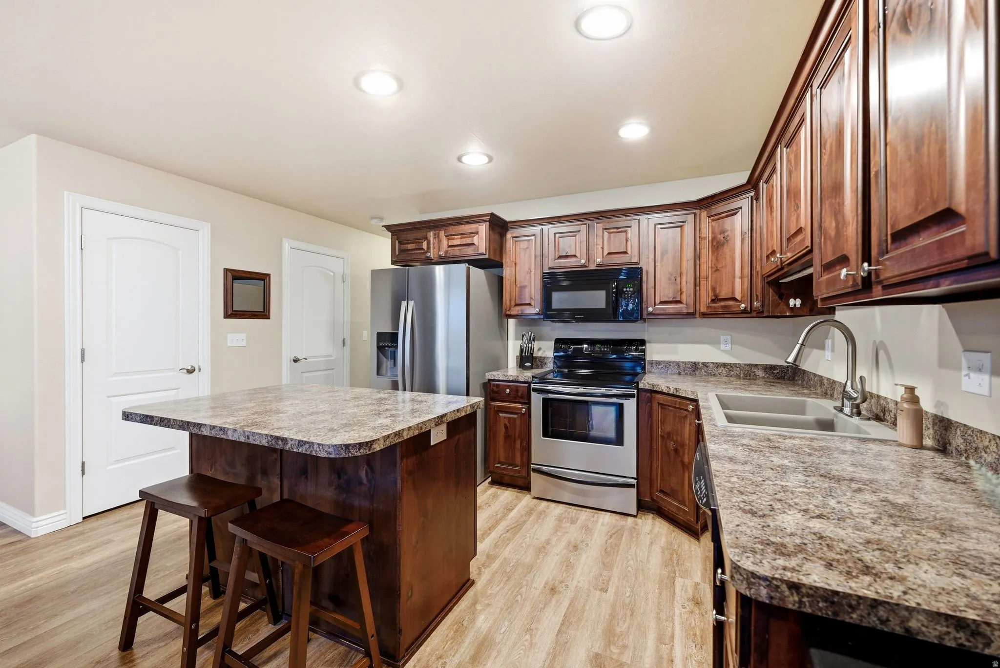 Kitchen featuring range, a kitchen breakfast bar, a center island, black microwave, and light wood-type flooring