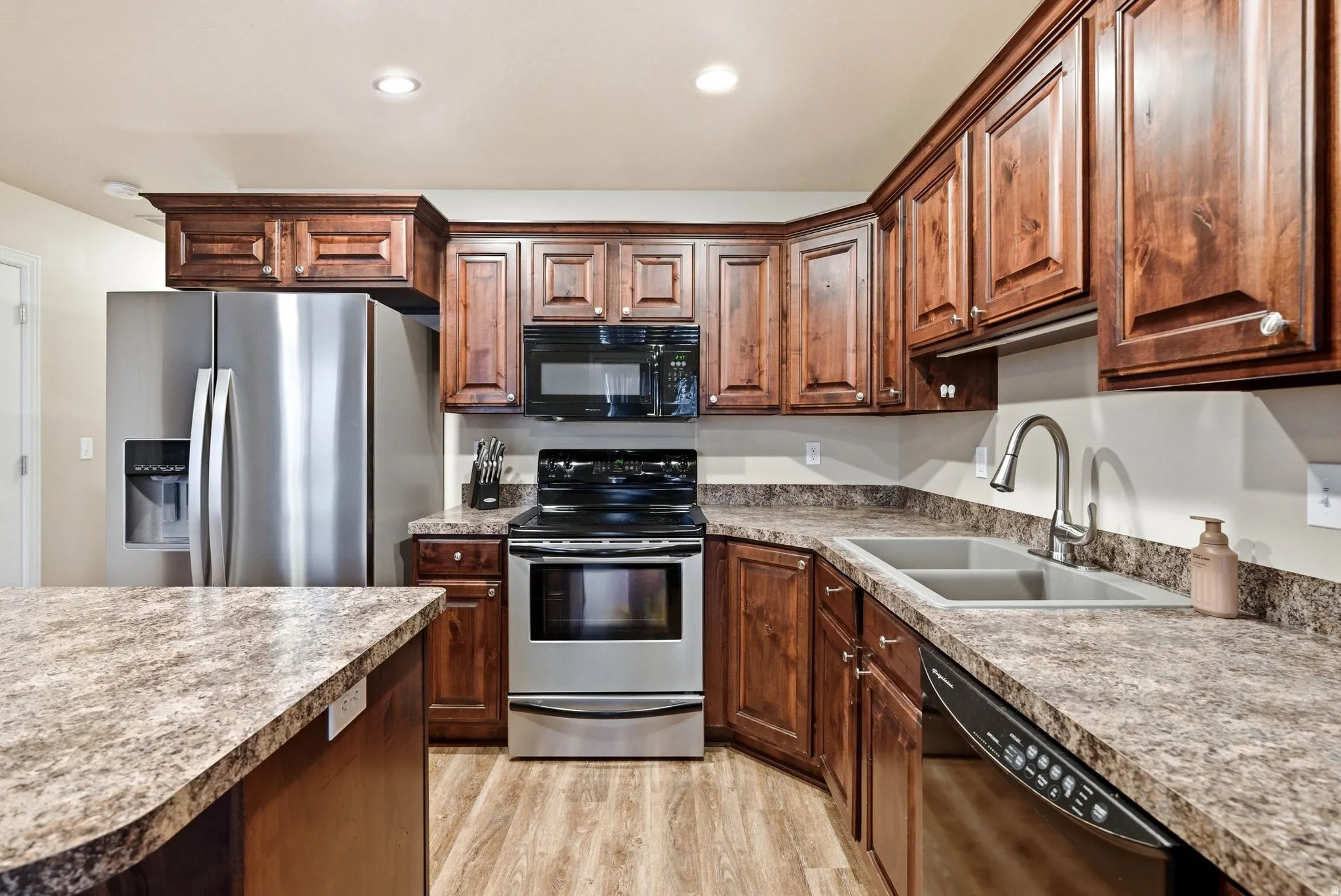 Kitchen featuring black appliances, light wood-style floors, recessed lighting, and light countertops