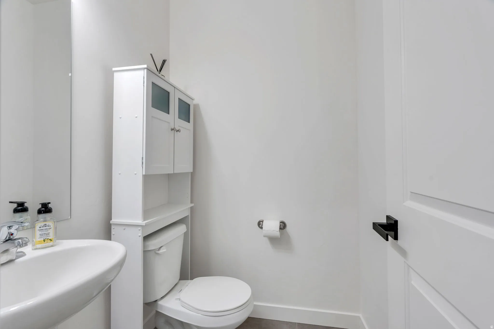 Pedestal sink with chrome faucet, white toilet, and over-toilet storage cabinet with frosted glass accents