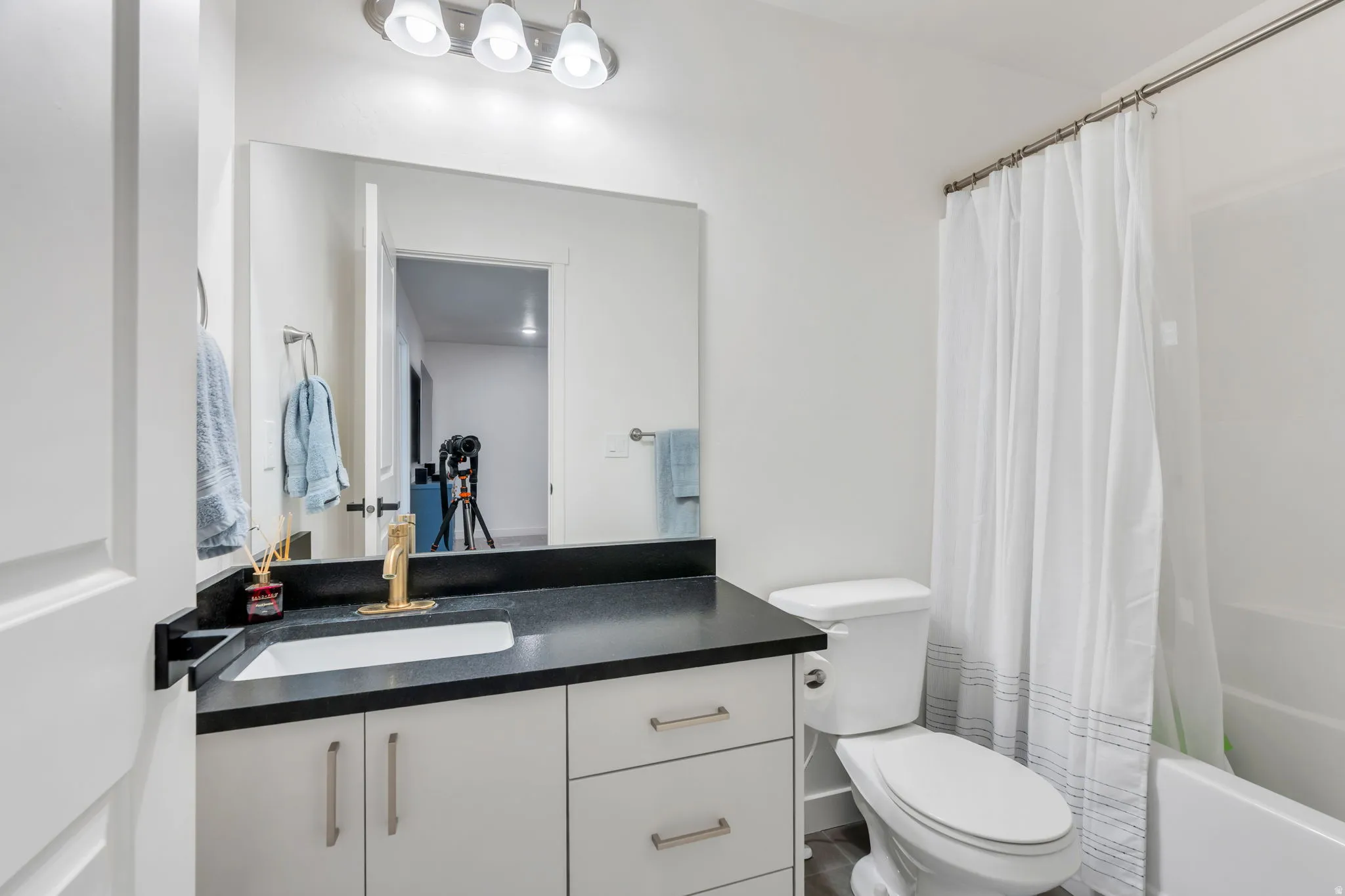 Bathroom featuring a white vanity with a dark countertop, an integrated sink, and a gold-finish faucet