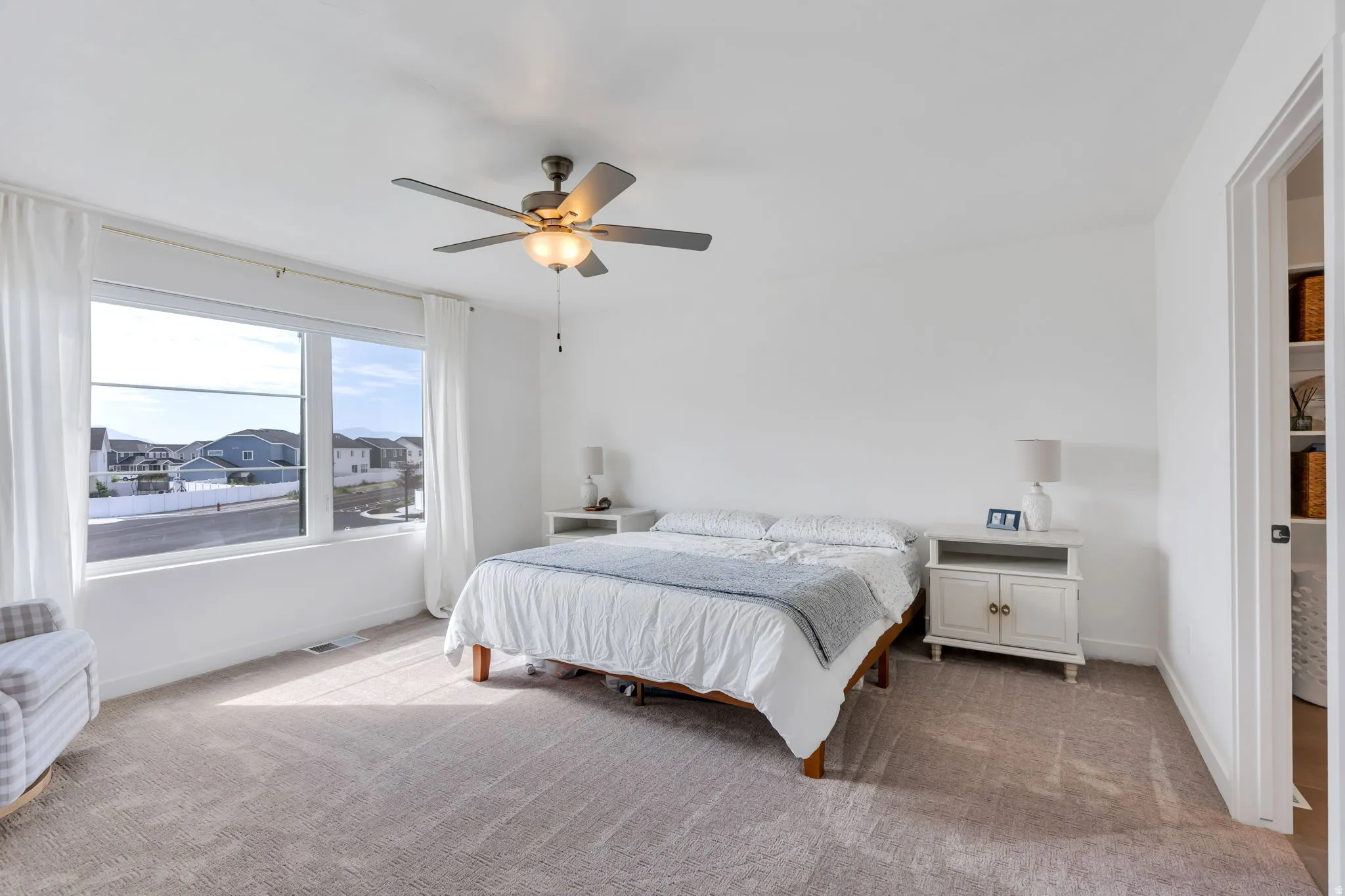 Spacious interior featuring a large window with white trim, a multi-speed ceiling fan with integrated lighting, plush neutral carpeting, and white painted walls