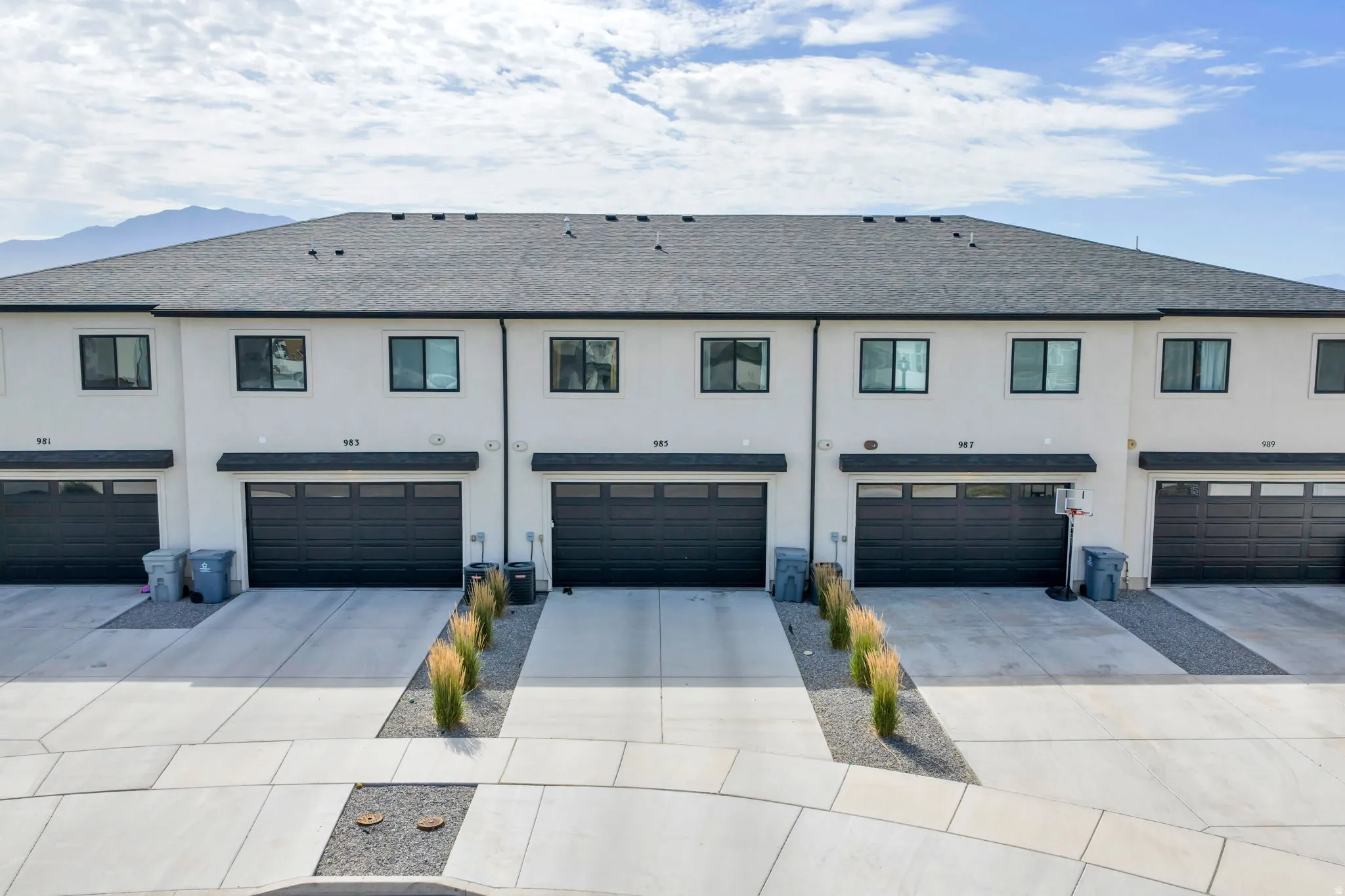 Modern townhome exteriors featuring light stucco finishes, dark garage doors, and black-framed windows