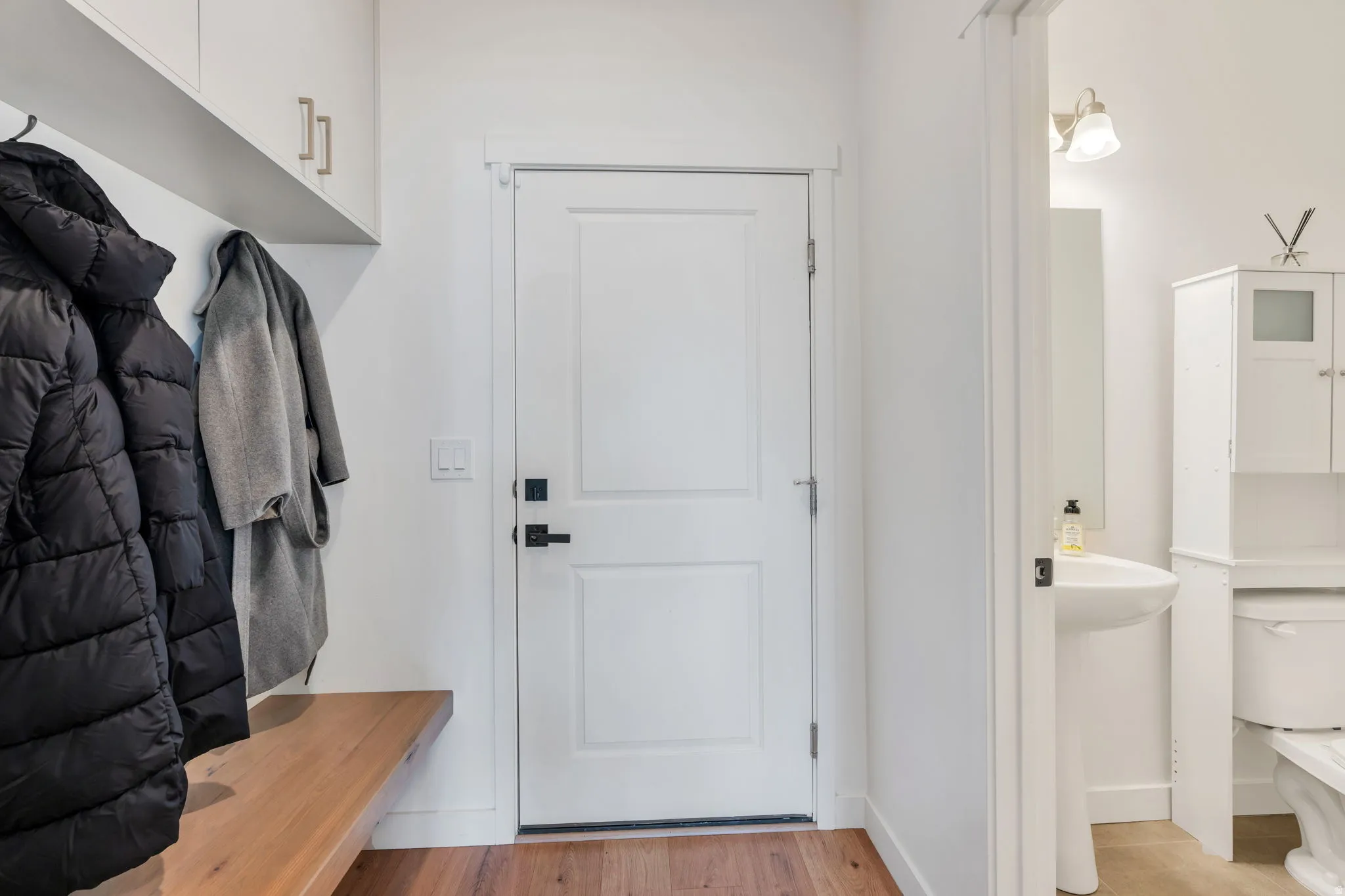 Entryway featuring wood-finish flooring, white paneled door with black hardware, and an integrated wood bench