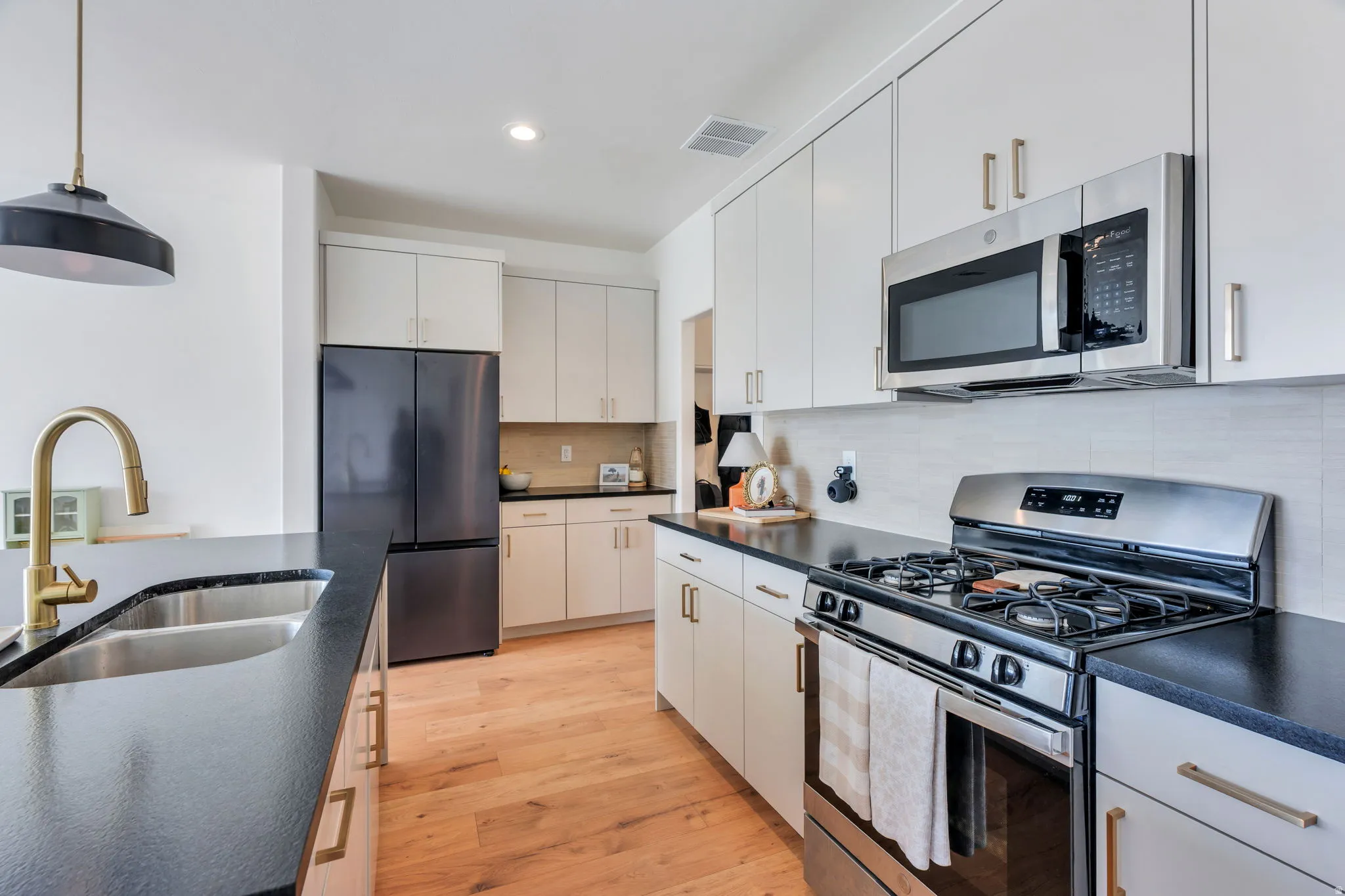 Modern kitchen with light wood-finish flooring, dark countertops, and white cabinetry