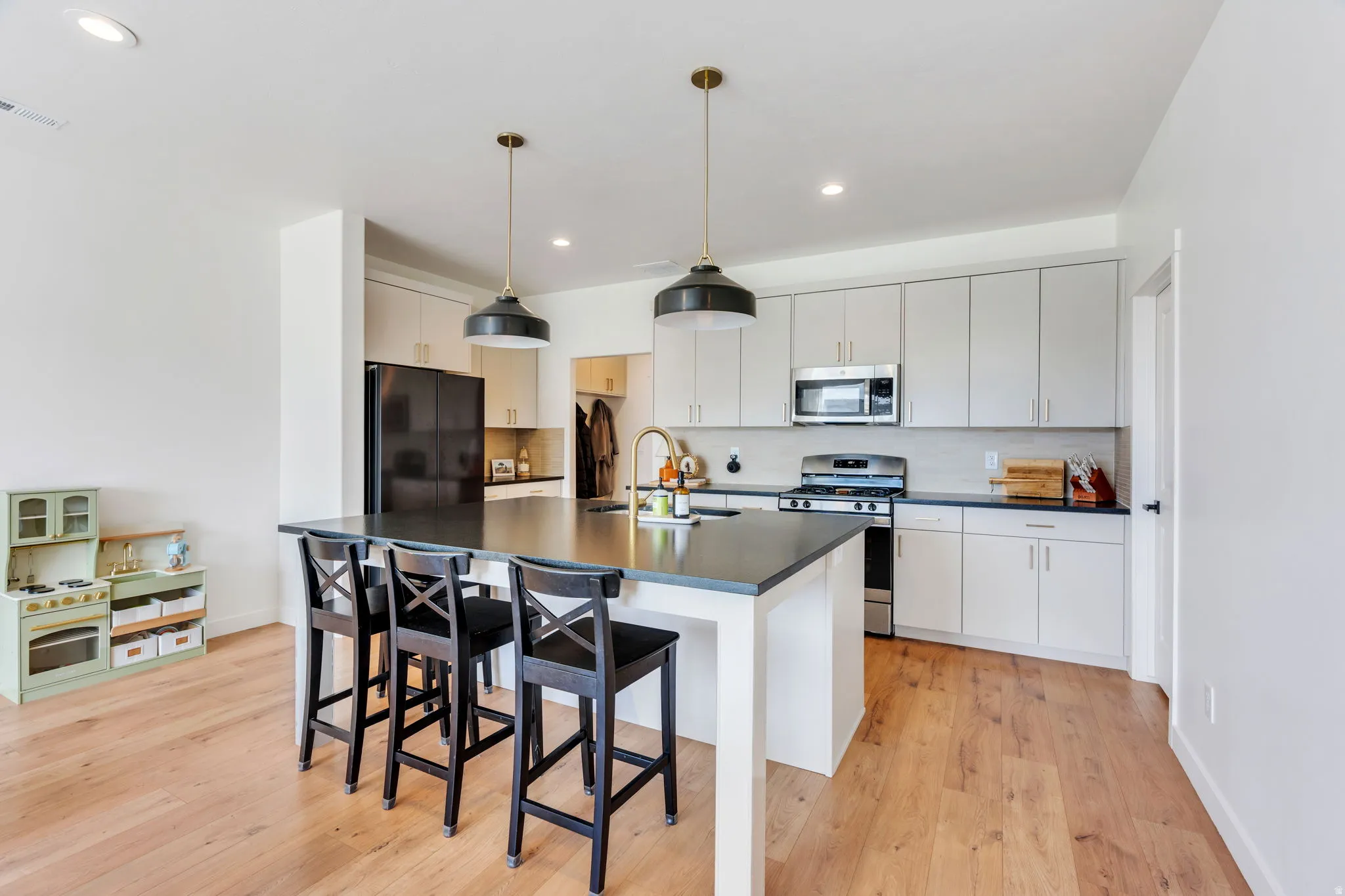 Kitchen featuring light wood-finish flooring, a central island with bar seating, gray cabinetry, stainless steel appliances, and two pendant lights