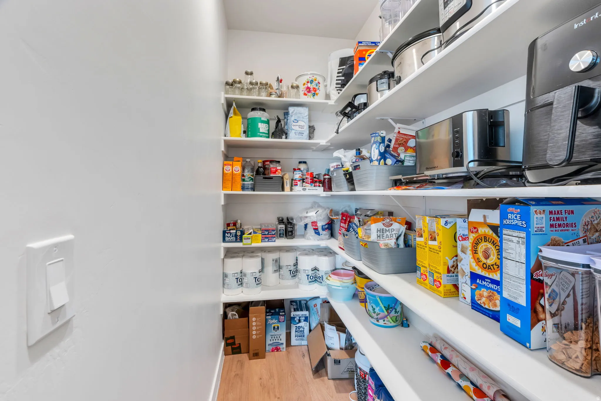 Walk-in pantry featuring white shelving, light wood-finish flooring, and white walls