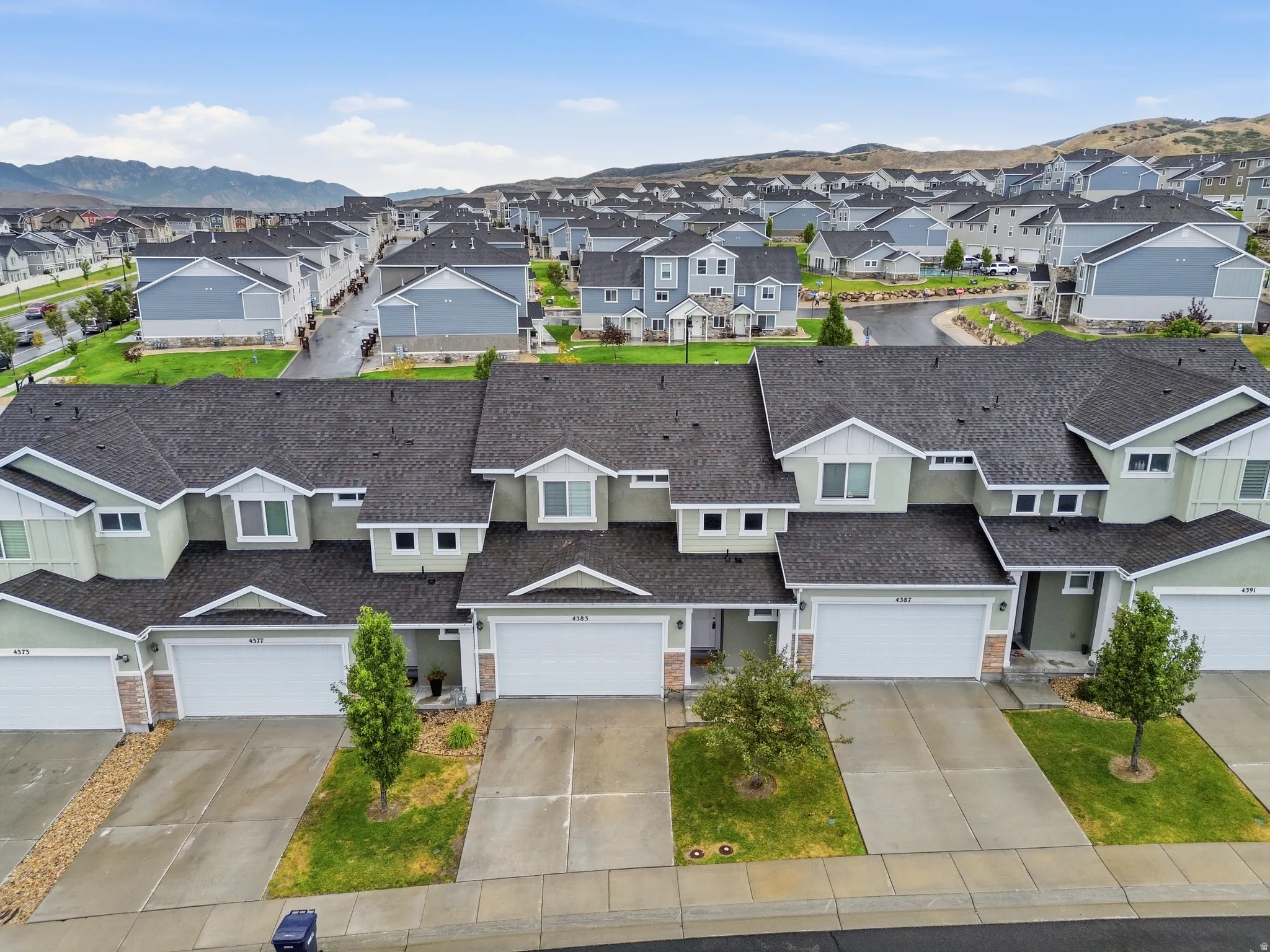 Contemporary townhome exteriors featuring light green siding, white trim, attached garages, and dormer windows