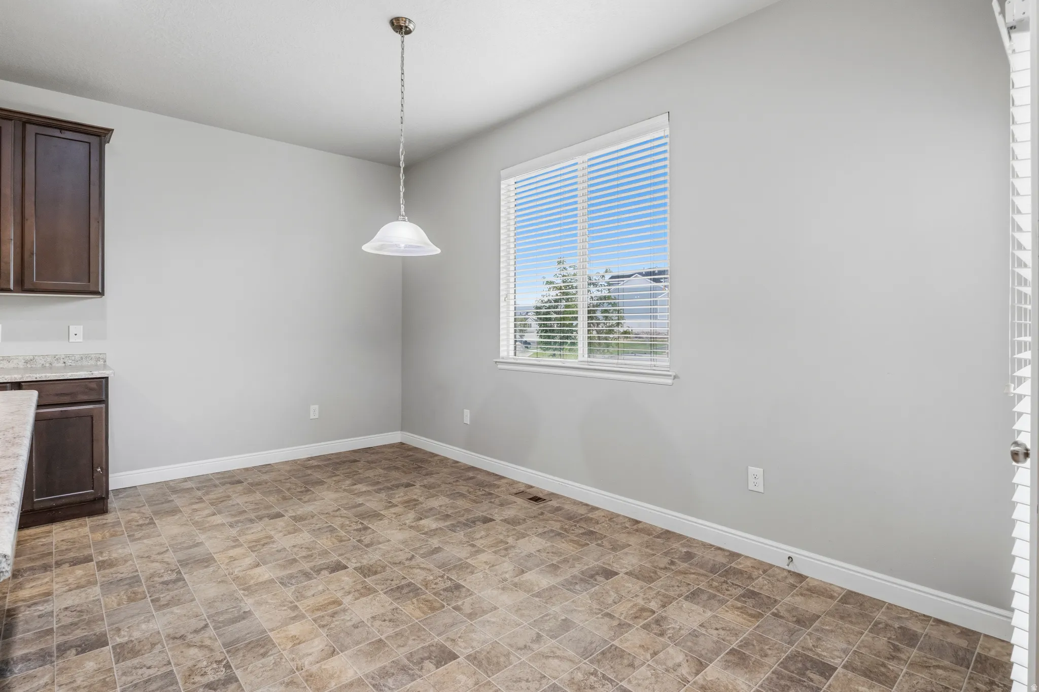 Dining area featuring a contemporary pendant light fixture, a large window with horizontal blinds, and durable tile flooring