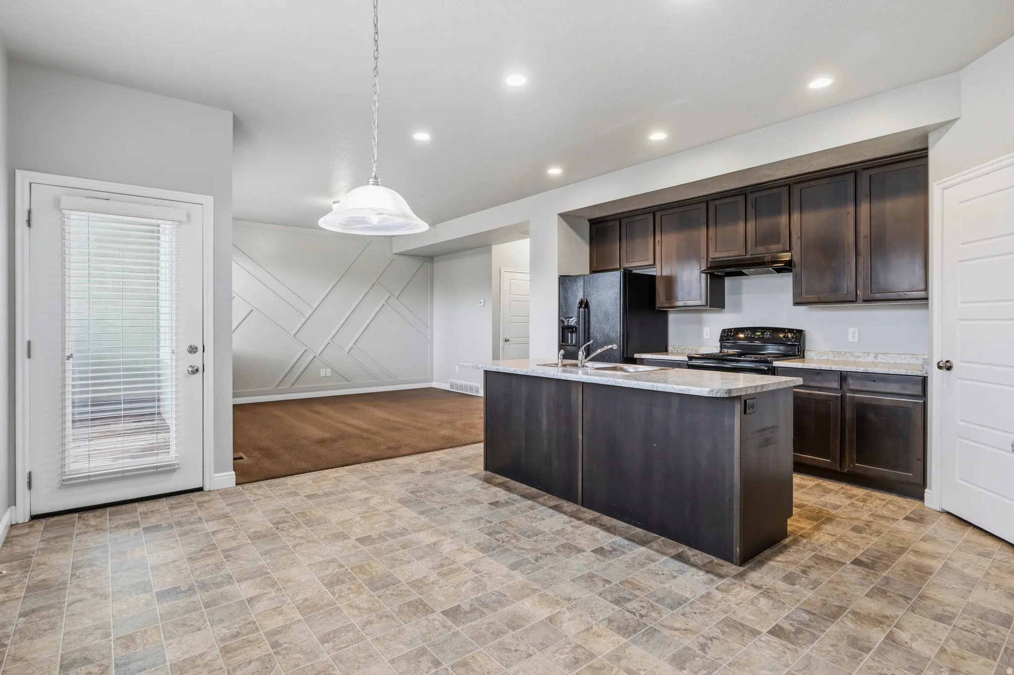 Open-concept kitchen featuring dark wood cabinetry, light-toned countertops, and a central island with integrated sink