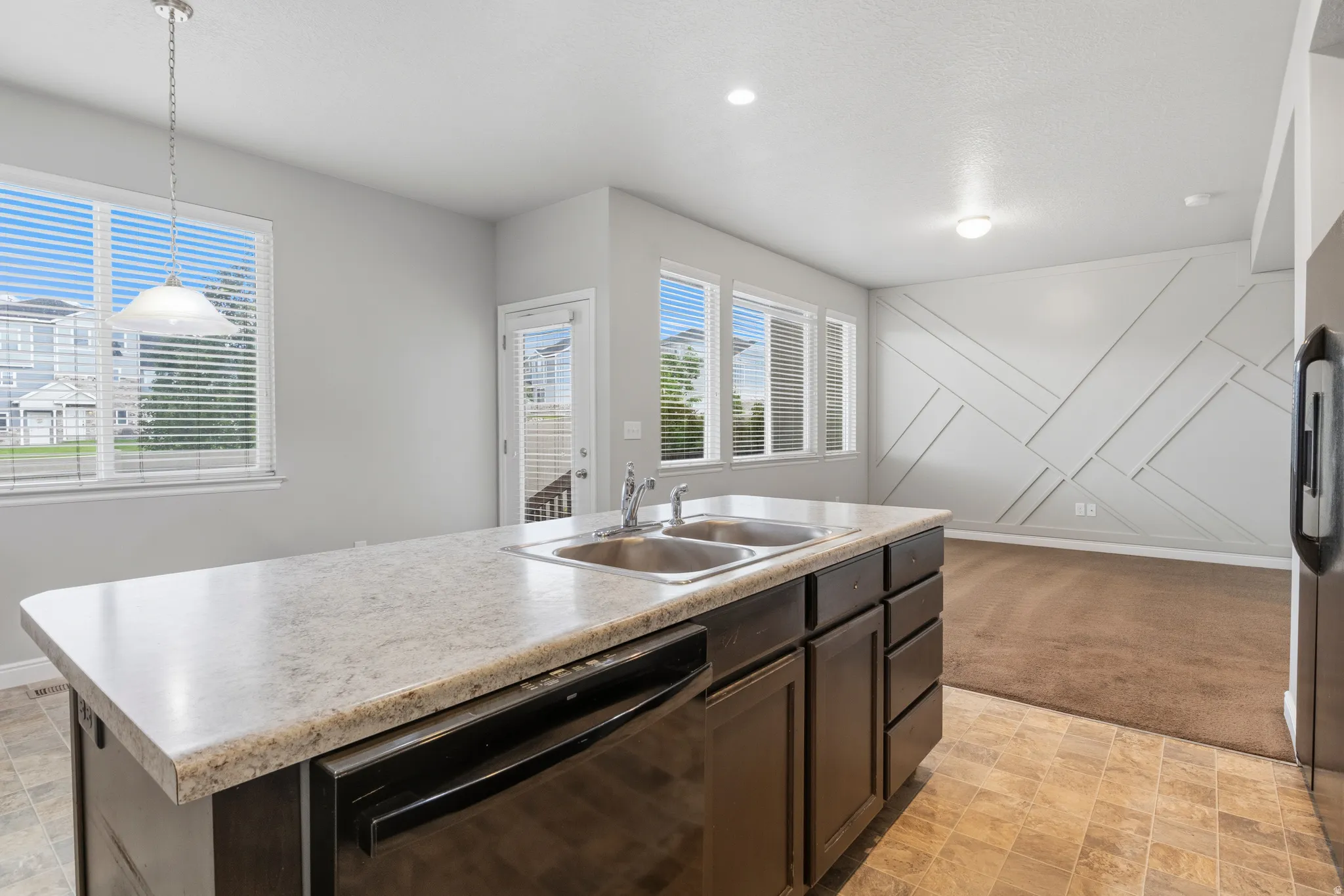 Kitchen island featuring a double-basin sink, integrated dishwasher, and light-toned countertop