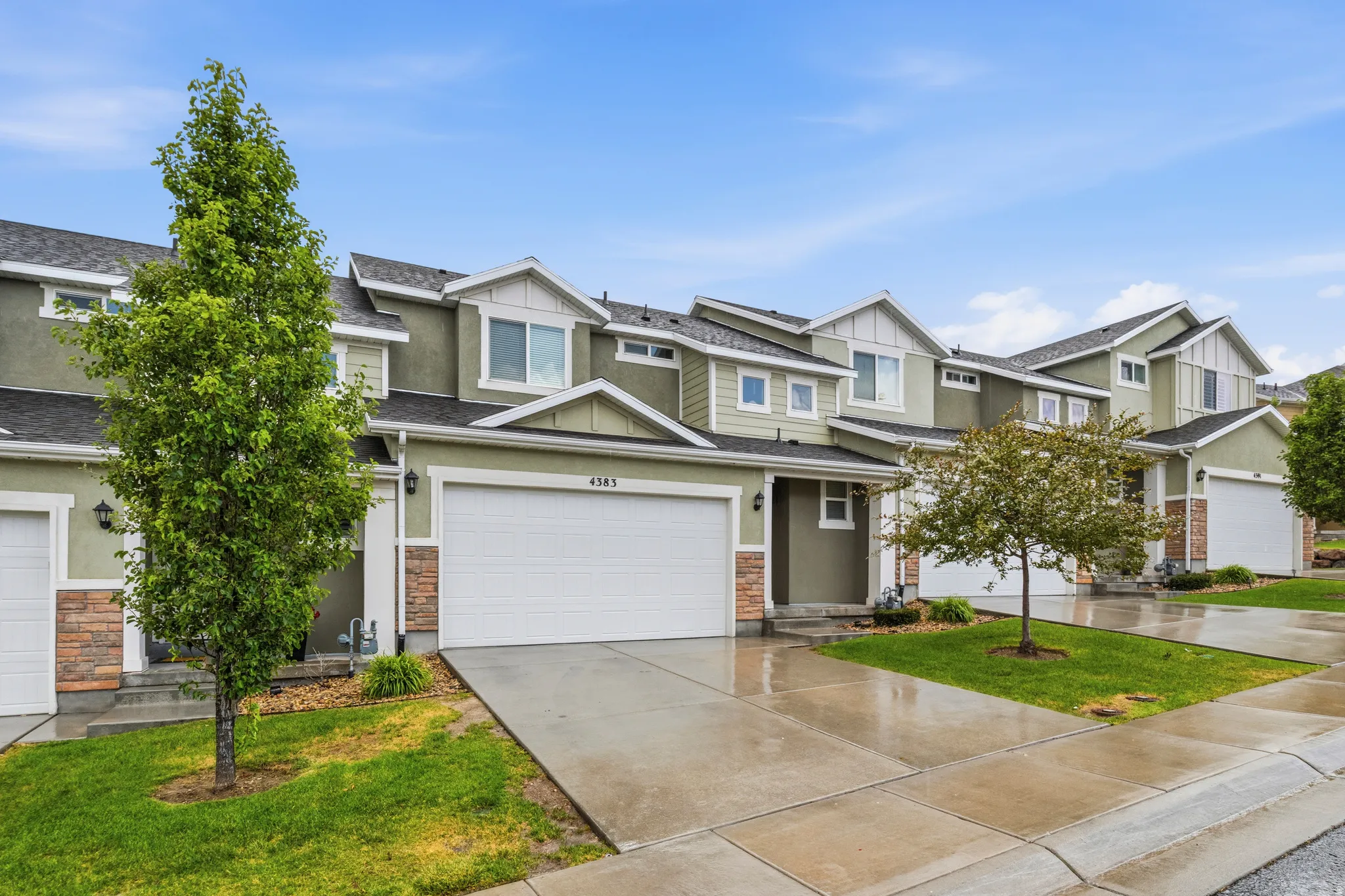 Townhome exterior featuring light green siding, white trim, and stone accents