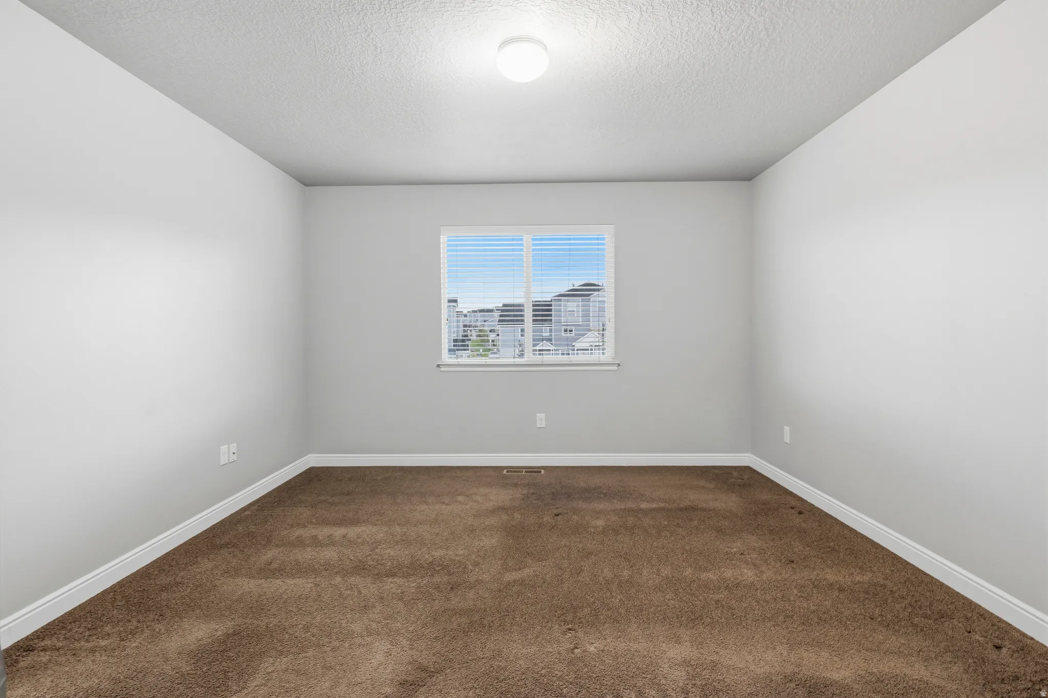 Carpeted room featuring a single window with blinds, a ceiling-mounted light fixture, and light gray painted walls with white baseboards