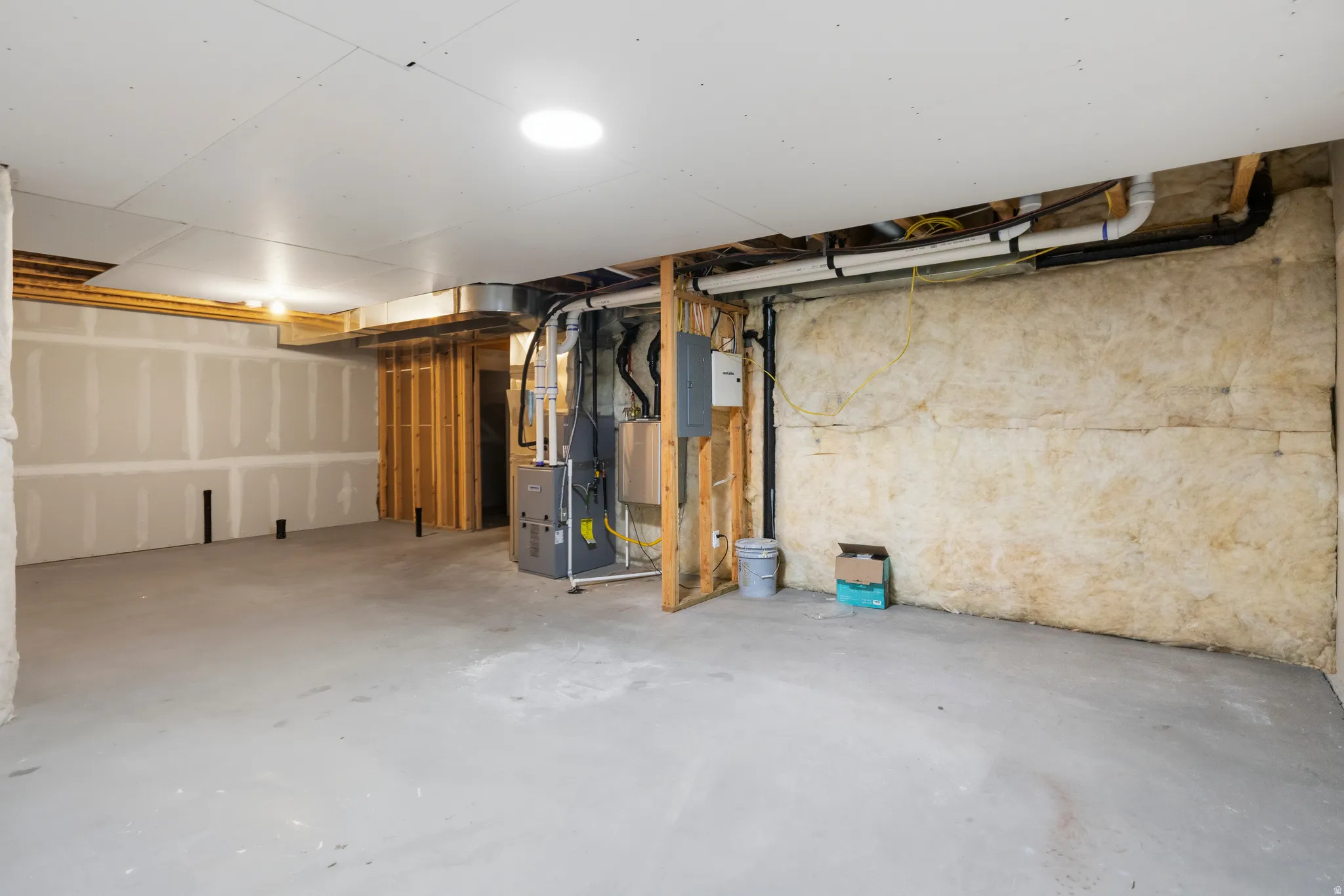 Unfinished basement featuring concrete flooring, partial drywall, exposed insulation, and visible utility systems