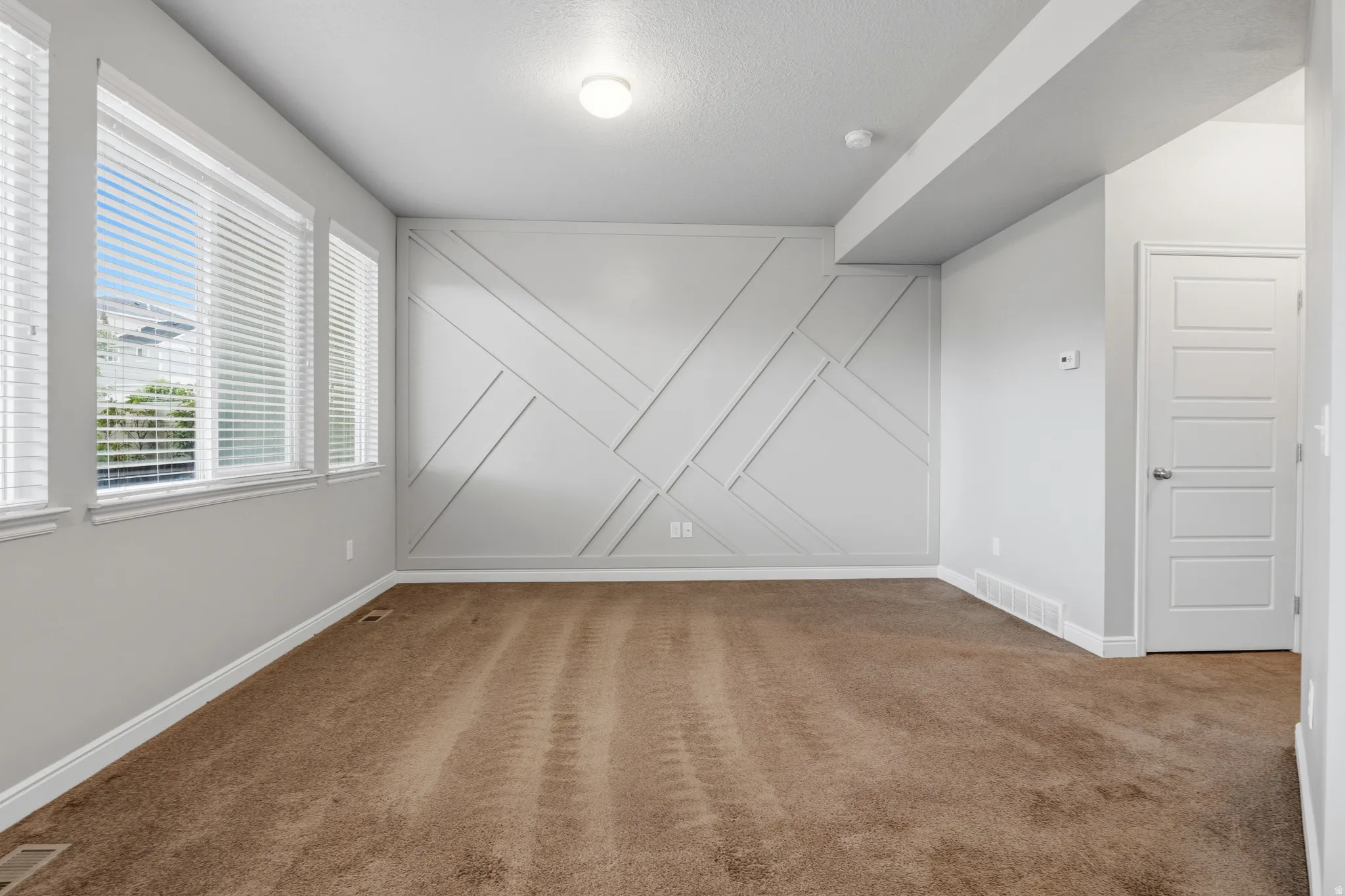 Spacious room featuring accent wall with geometric molding, brown carpeting, and multiple windows with white blinds
