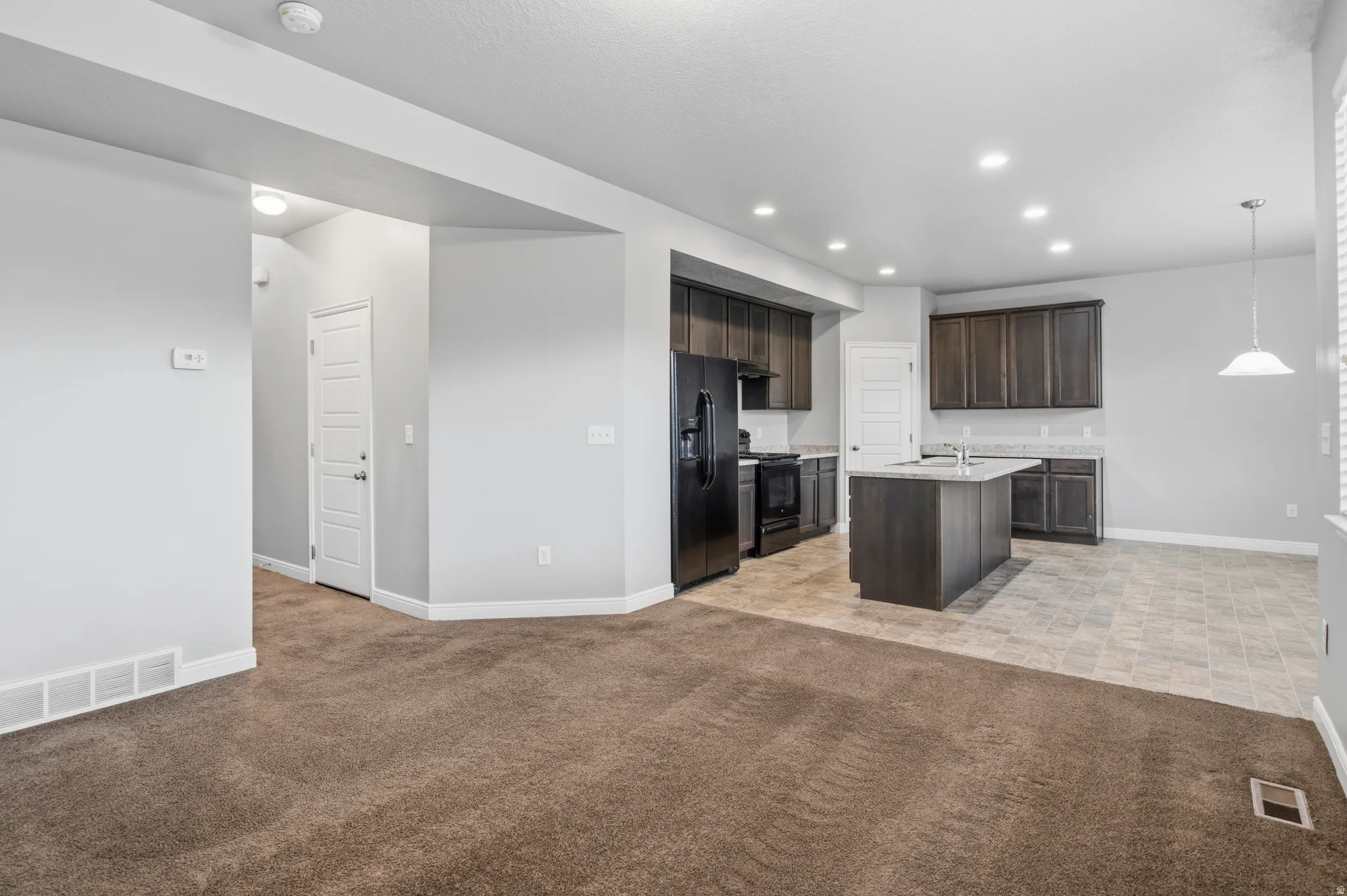 Open-concept living space featuring a kitchen with dark cabinetry, black appliances, and an island with a sink