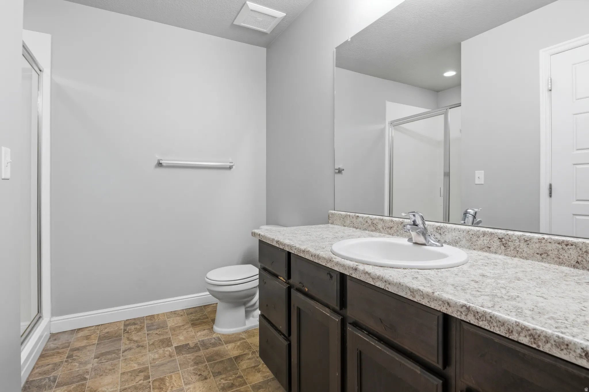 Master Bathroom featuring a dark wood-finish vanity with a light speckled countertop, an undermount sink with chrome fixtures, a large mirror, and a shower with a sliding glass door