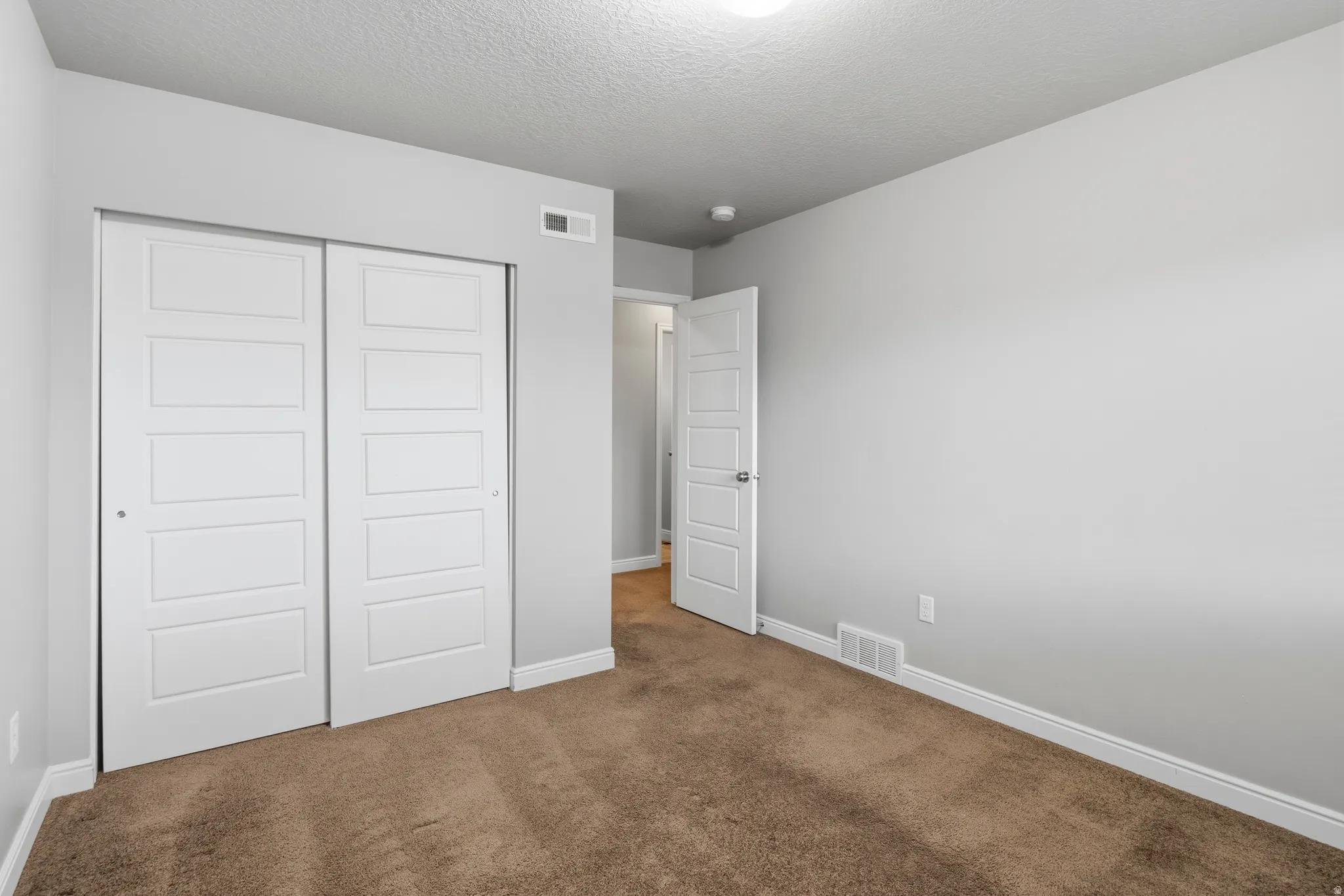 Bedroom featuring light gray wall paint, brown carpet flooring, white baseboards, and a white interior door with panel detailing