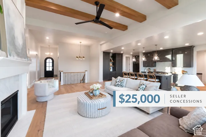 Spacious open-concept living area featuring exposed ceiling beams, wood-finish flooring, a fireplace with a light-toned surround, a staircase with wood railing, and a kitchen with dark cabinetry