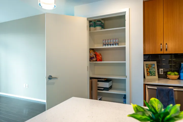 Built-in pantry with multiple shelves, adjacent to hardwood-finish cabinetry, a black subway tile backsplash, and a stainless steel appliance
