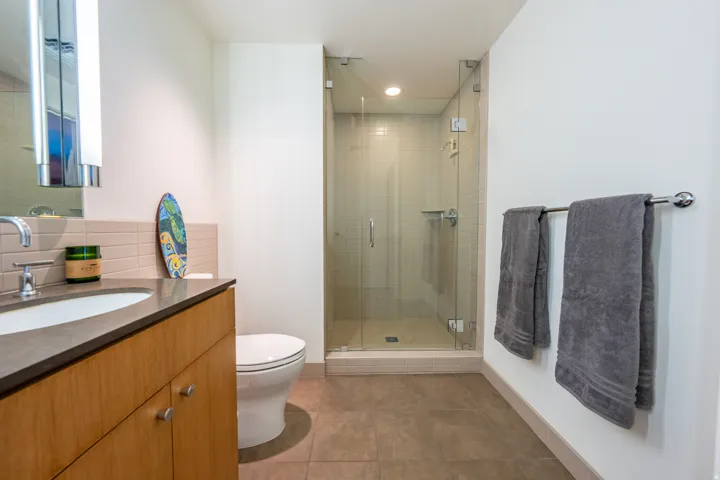 Bathroom featuring a wood vanity with integrated sink, rectangular mirror with sconce lighting, glass-enclosed shower, and tile flooring