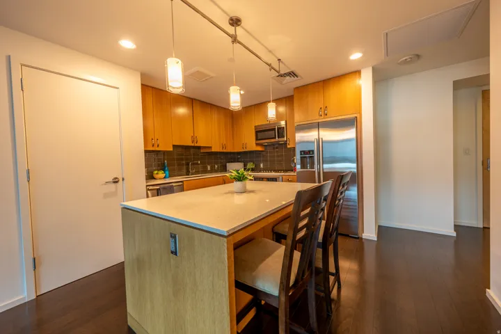 Kitchen featuring wood cabinetry, stainless steel appliances, a stone countertop island, track lighting with pendant fixtures, and dark wood-finish flooring