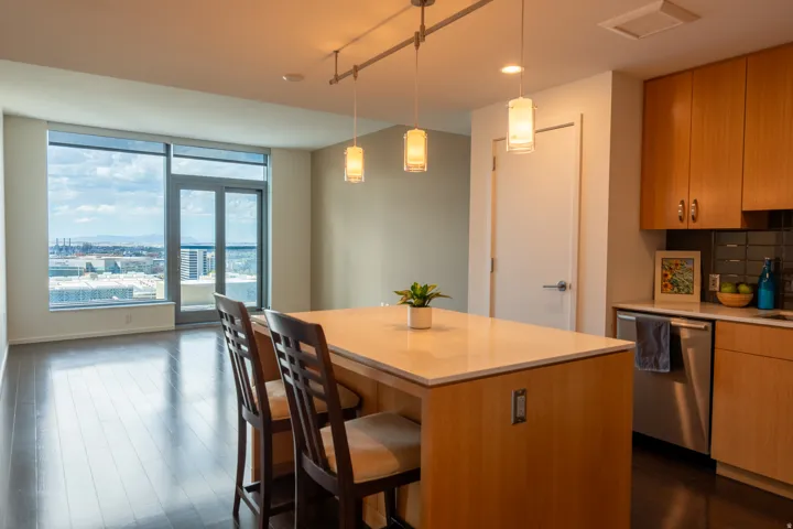 Open-concept kitchen with wood-finish flooring, light wood cabinetry, and a light-toned island countertop