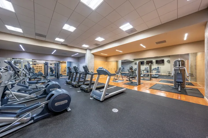 Fitness center with a variety of exercise equipment, mirrored wall, wood-finish flooring, and recessed lighting