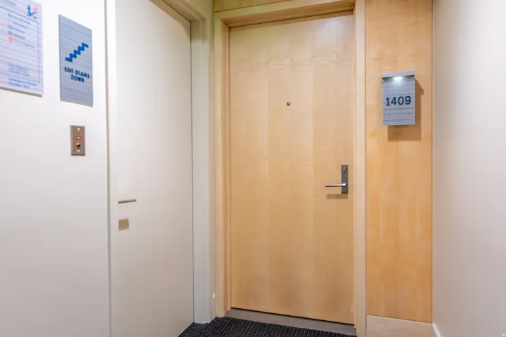 Light wood-finish door with a contemporary handle, complemented by a modern illuminated unit number display