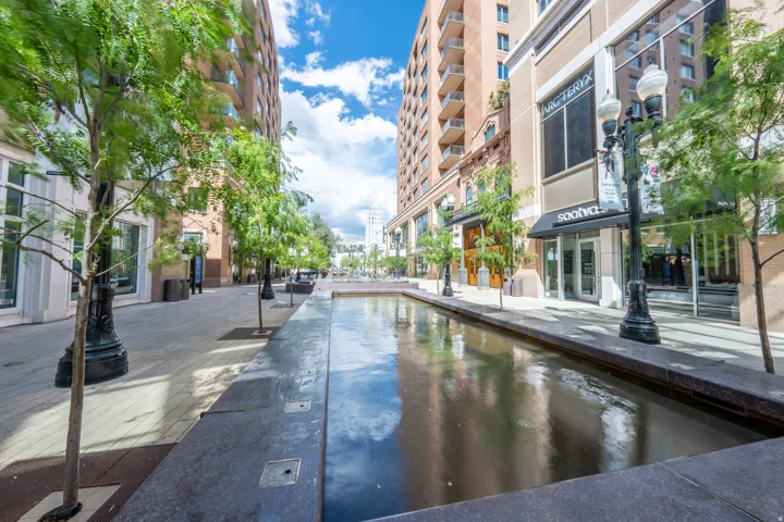 Pedestrian-friendly streetscape featuring a water feature, mature trees, and multi-story buildings with commercial storefronts
