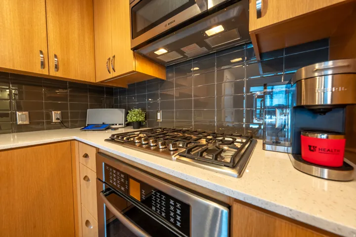 Wood cabinetry with stainless hardware, light-toned countertops, tile backsplash, built-in stainless steel microwave, and gas range with oven