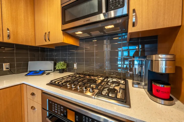 Wood-finish cabinetry paired with a light-toned countertop, stainless steel gas cooktop, and built-in microwave