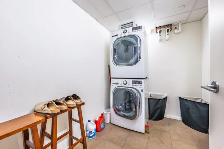 Laundry area featuring a stackable washer and dryer, tile flooring, and a drop ceiling