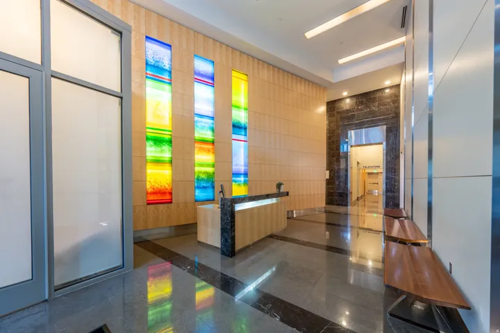 Polished stone flooring, wood-finish wall paneling, built-in reception desk with stone countertop, integrated colorful glass panels, and recessed ceiling lighting