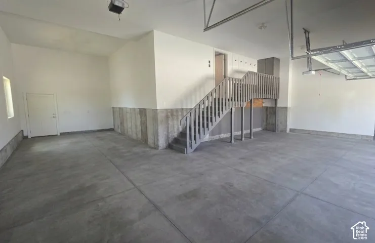 Spacious garage featuring a concrete floor, painted white walls, and a finished staircase with wooden railings