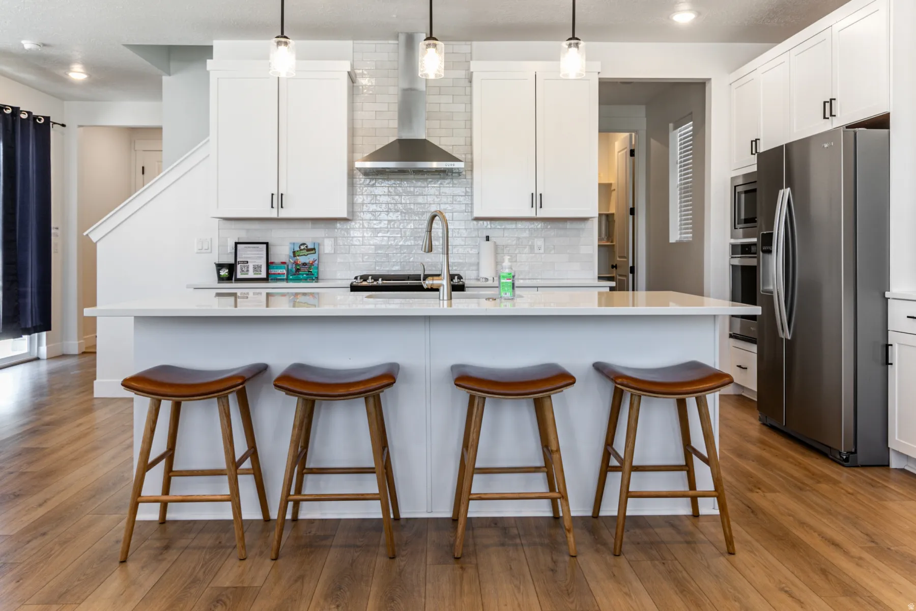 Open-concept kitchen featuring an expansive island with seating, white shaker cabinetry, stainless steel appliances, and wood-finish flooring