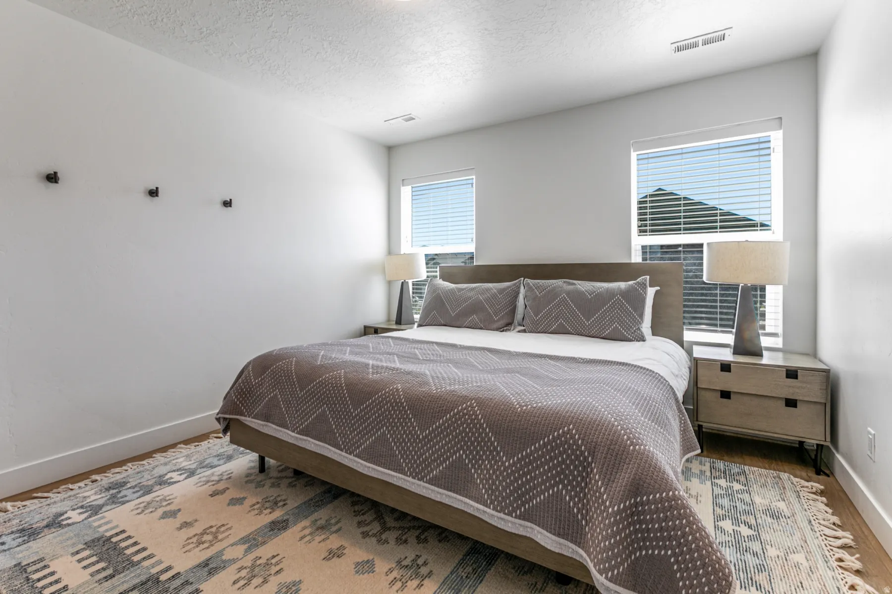 Bedroom featuring two windows with blinds, light-colored walls, wood-finish flooring, and recessed ceiling lighting