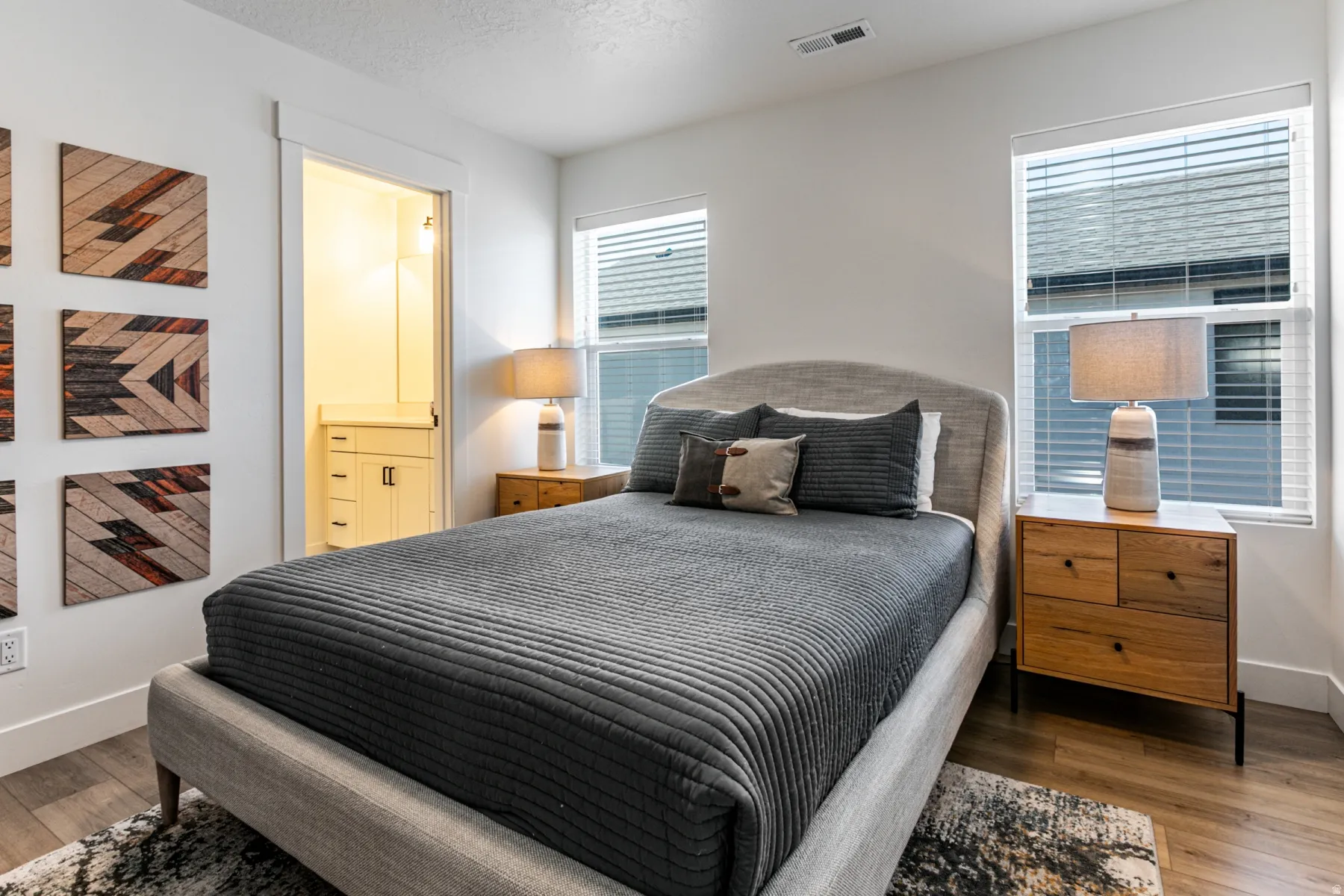 Bedroom featuring wood-finish flooring, white baseboards, and two windows with horizontal blinds
