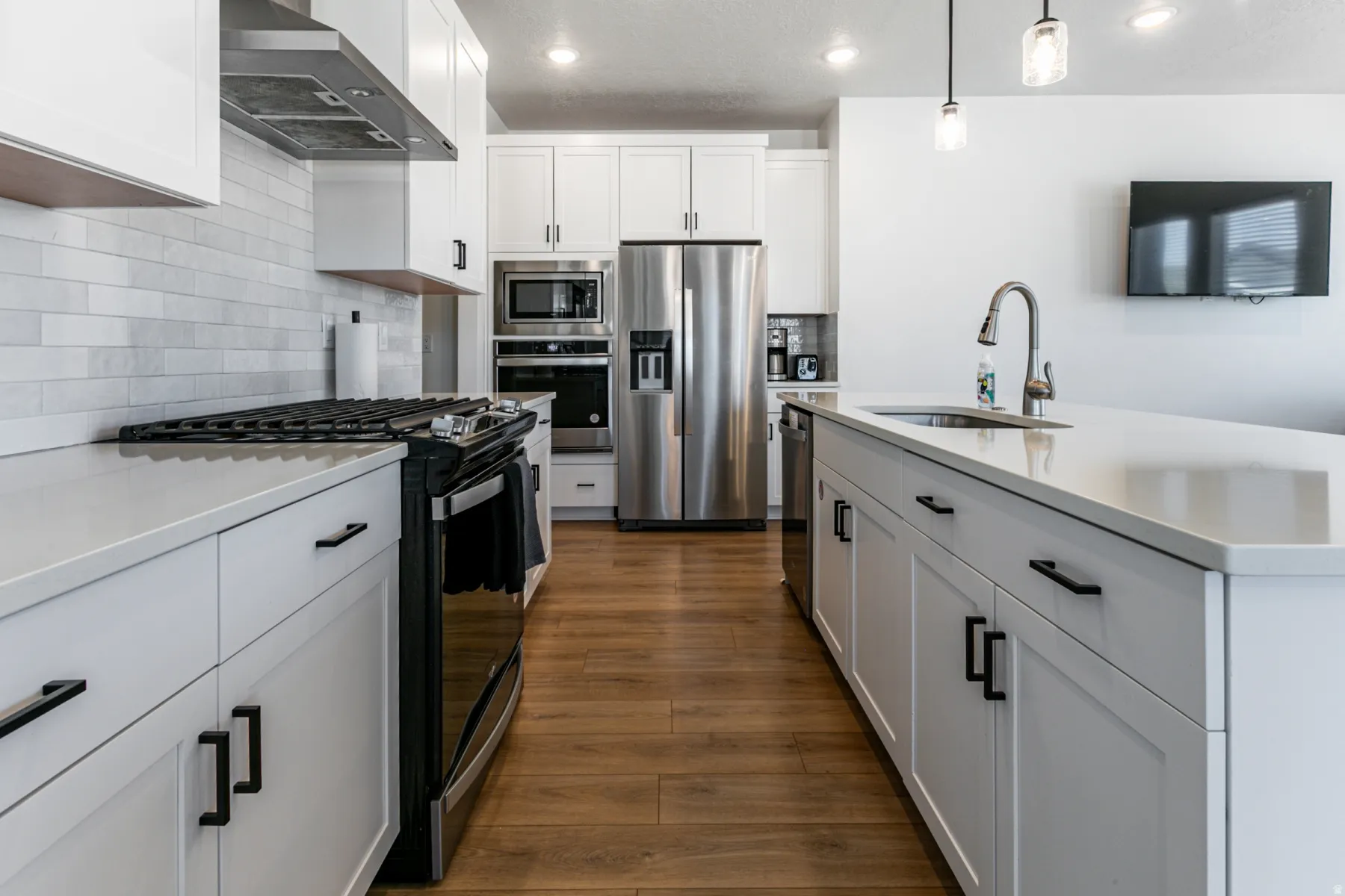 Modern kitchen featuring wood-finish flooring, white cabinetry with black hardware, stainless steel appliances, a subway tile backsplash, and a large island with an undermount sink
