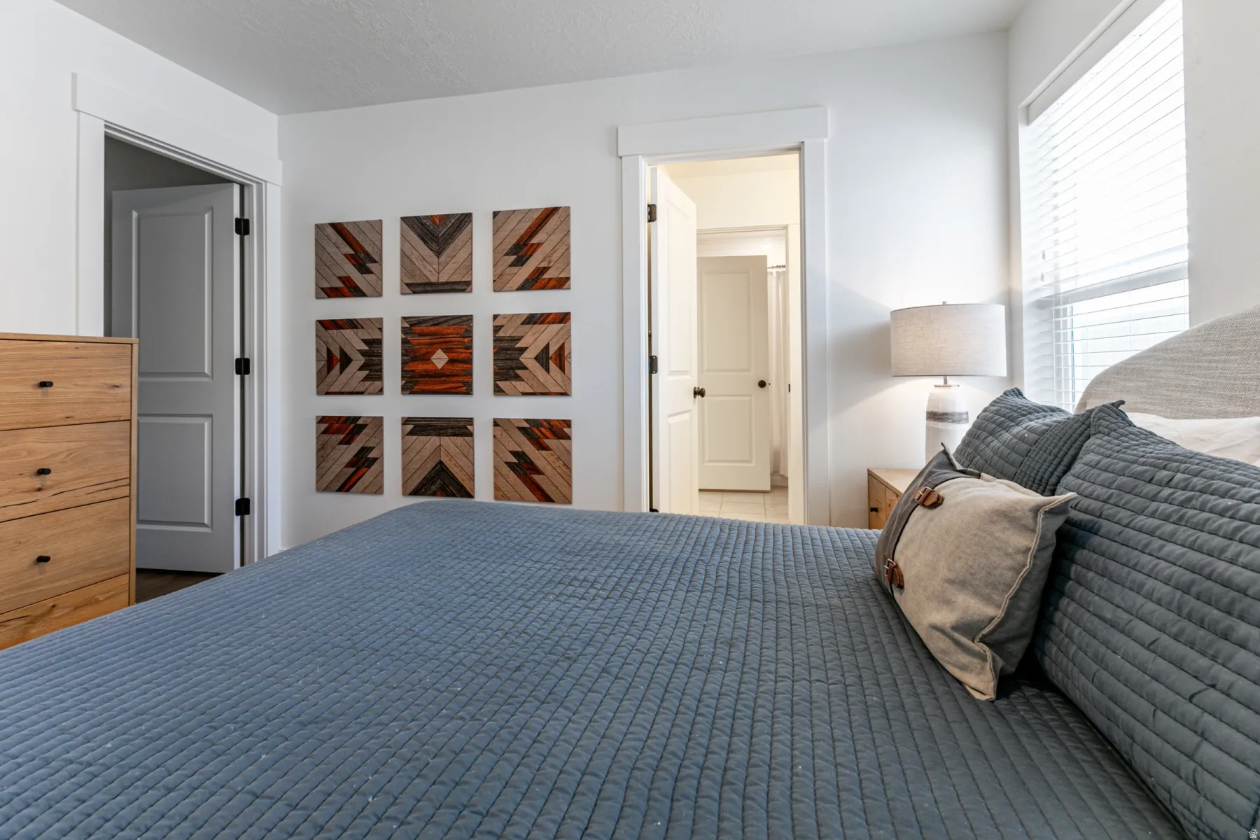 Bright bedroom featuring white walls, a window with horizontal blinds, and a flat-panel interior door with matte black hardware