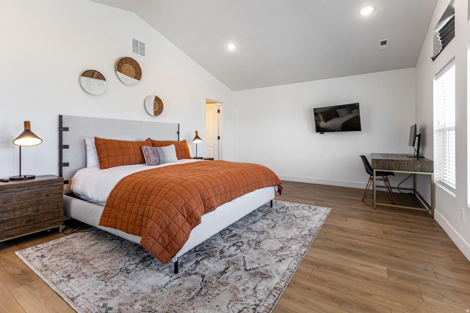 Spacious room featuring vaulted ceilings, wood-finish flooring, recessed lighting, and ample natural light from multiple windows