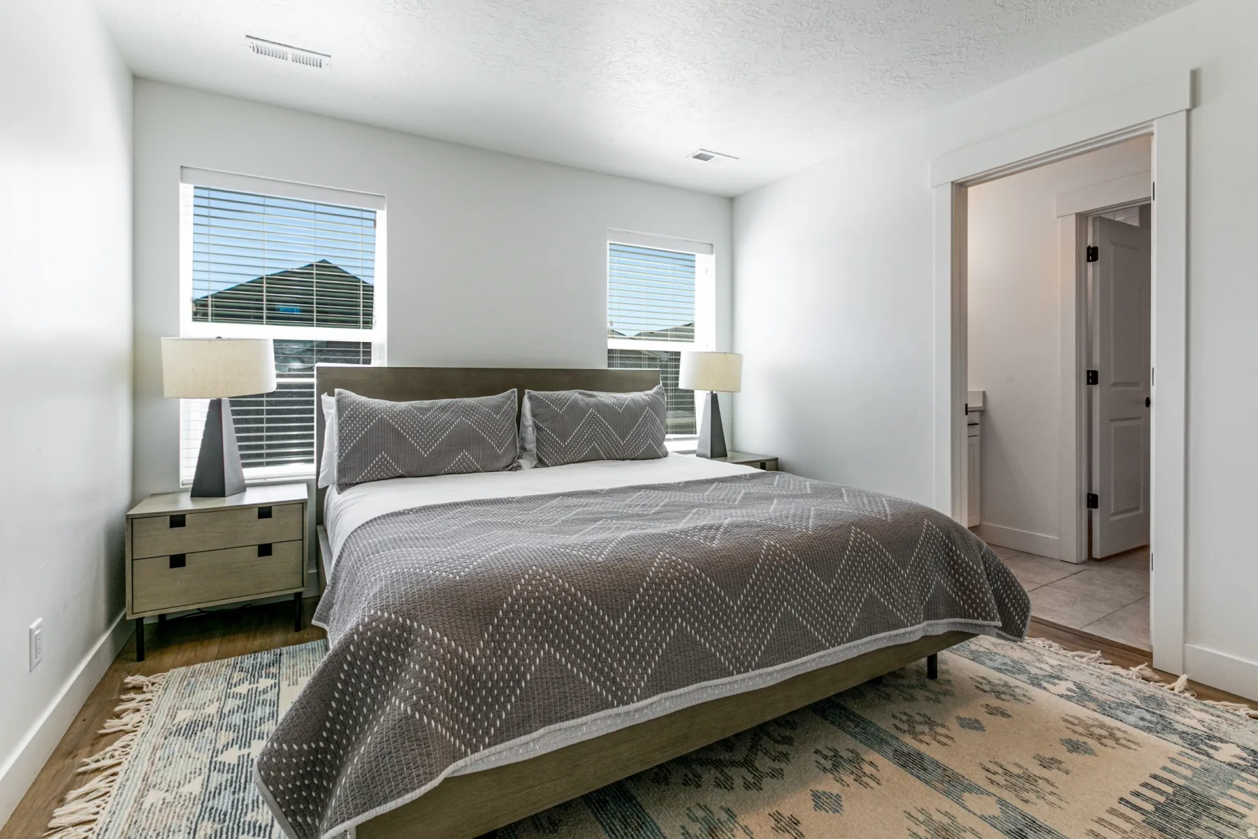 Bright bedroom featuring two windows with blinds, white trim, and wood-finish flooring