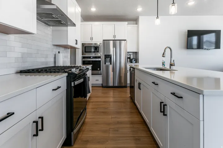 Modern kitchen featuring wood-finish flooring, white cabinetry with black hardware, stainless steel appliances, a subway tile backsplash, and a large island with an undermount sink