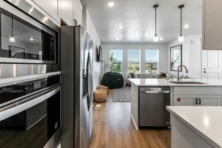 Kitchen and living area featuring stainless steel appliances, white cabinetry, wood-finish flooring, quartz countertops, and three large windows