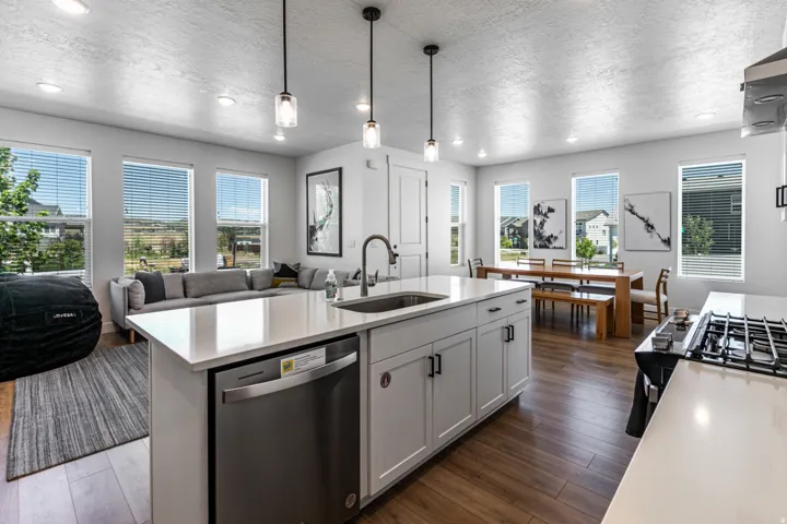 Open-concept kitchen featuring a large island with an undermount sink, stainless steel dishwasher, and pendant lighting